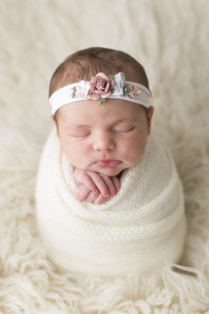 Séance photo d'un nouveau-né emmailloté dans un linge blanc.