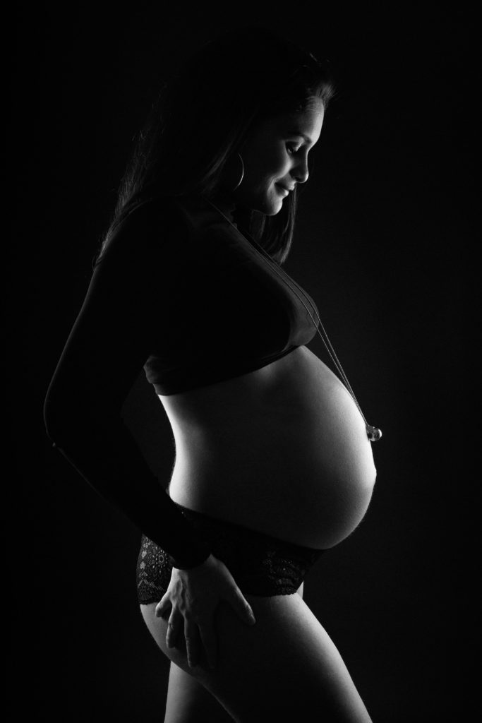 Séance grossesse sur fond noir d'une maman regardant son ventre arrondi.