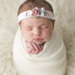 Séance photo d'un nouveau-né emmailloté dans un linge blanc.