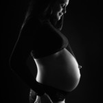 Séance grossesse sur fond noir d'une maman regardant son ventre arrondi.